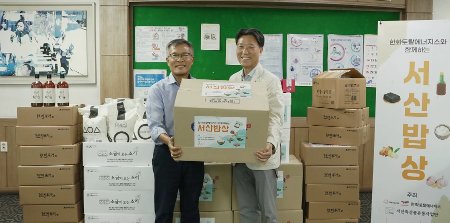 25일 한화토탈에너지스 관계자(오른쪽)가 고객사 ㈜우성케미칼 박병욱 대표이사(왼쪽)에게 농수산물을 전달하는 모습